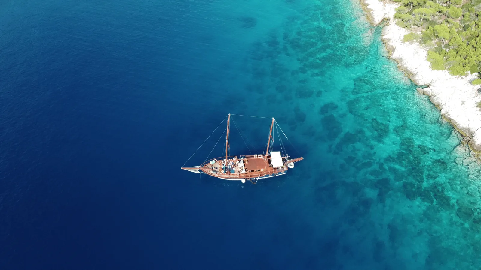 A wooden cruise boat beside the turquoise Saronic coast